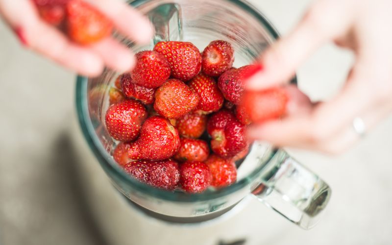 Blender vu de près d'en haut, dans lequel une personne mets des fraises.